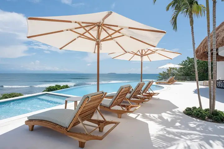 Teak loungers under white umbrellas beside the pool, the bay behind